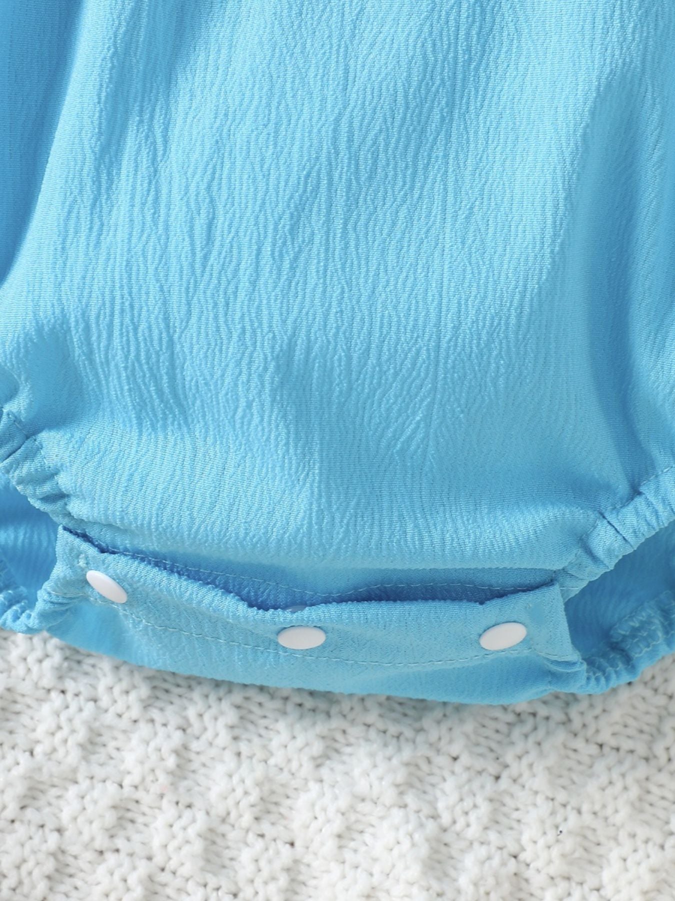Pastel blue cotton baby romper with textured fabric and white snap closure.