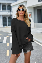 Black acrylic knit sweater with flared sleeves and slit hem detail.