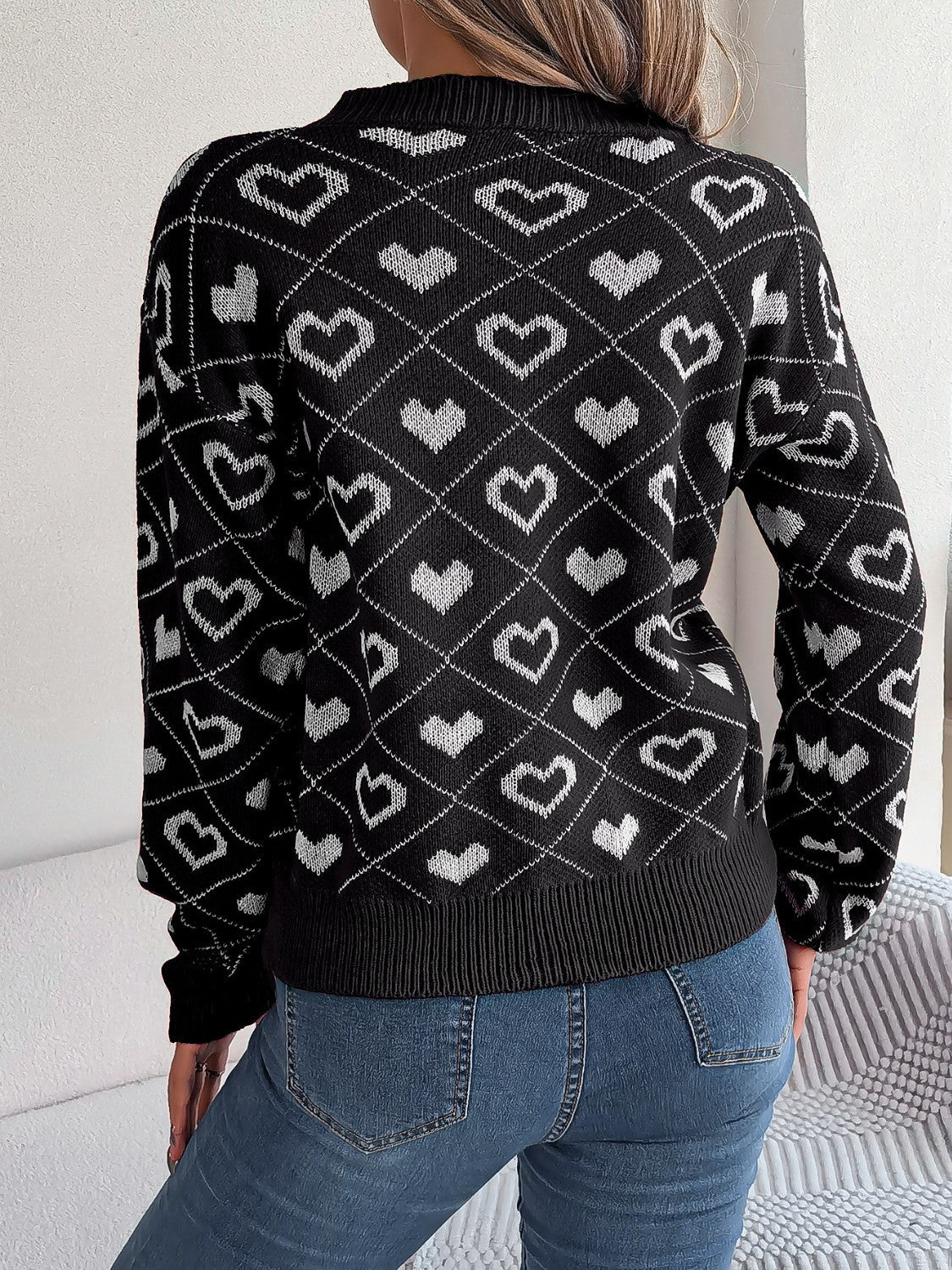 Black acrylic knit sweater with allover white heart jacquard pattern and V-neck.
