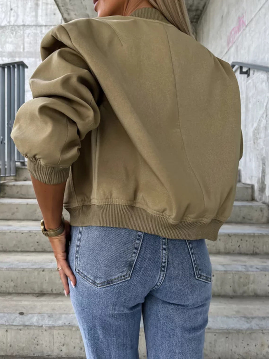Olive bomber jacket with sculpted sleeves and ribbed cuffs, styled with jeans.