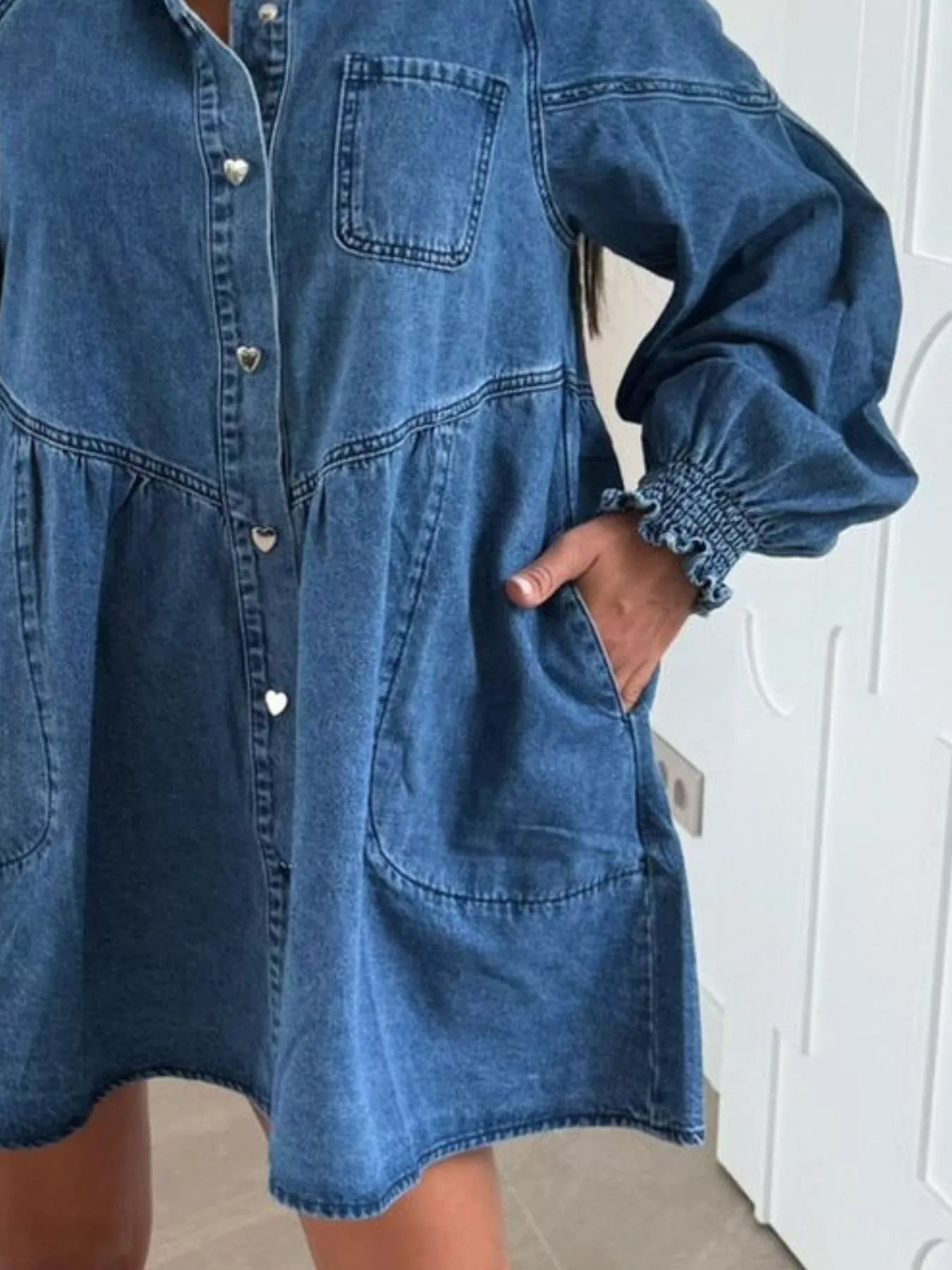 Blue denim mini dress with pockets, button front, and smocked cuffs.