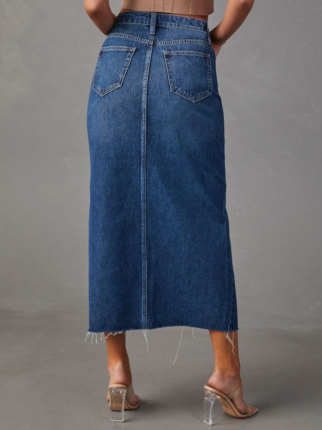 Denim midi skirt in dark wash with raw hem and buttoned closure.