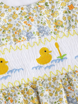 Baby one-piece with floral print, smocked white panel, and embroidered yellow ducks in water.
