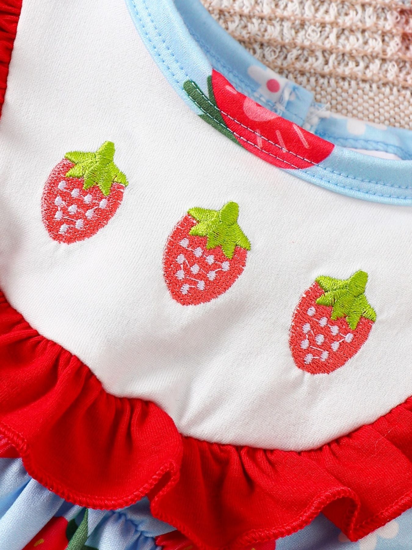 Baby one-piece with embroidered strawberries, red ruffles, and blue floral print.