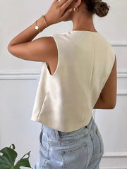 Cream button-down sleeveless vest with crew neck and cropped length, styled with jeans.