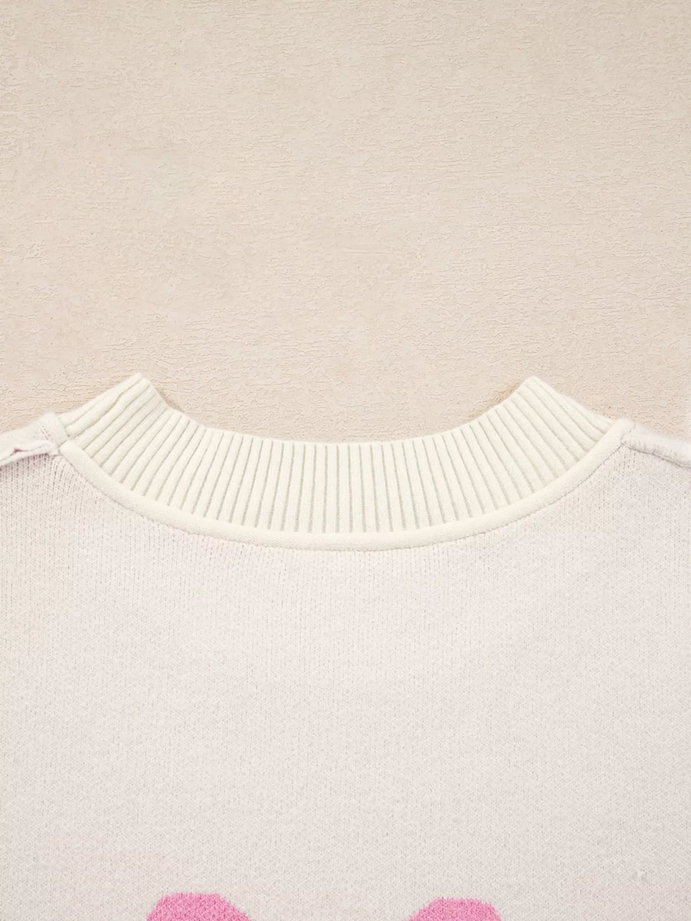 Beige acrylic blend sweater with pink bow print and ribbed crew neck.