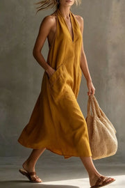 Mustard halter midi dress with pockets and V-neckline, shown on a model walking.