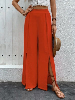 Orange-red textured palazzo trousers with dramatic thigh-high slits and wide legs.