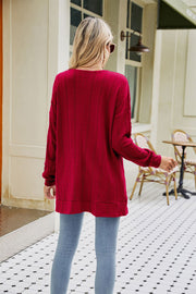 Wine cable-knit cardigan with chevron pattern and long sleeves, worn with jeans.