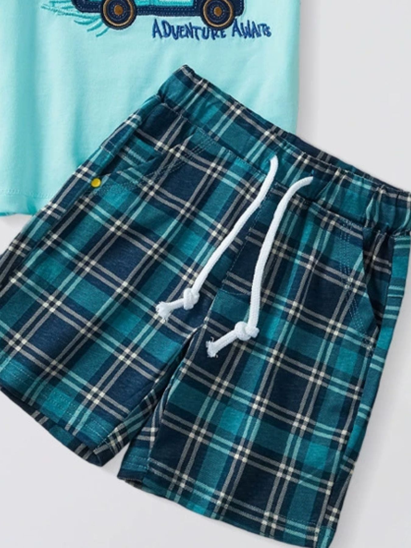Toddler graphic tee with "Adventure Awaits" text and blue plaid shorts with drawstring.