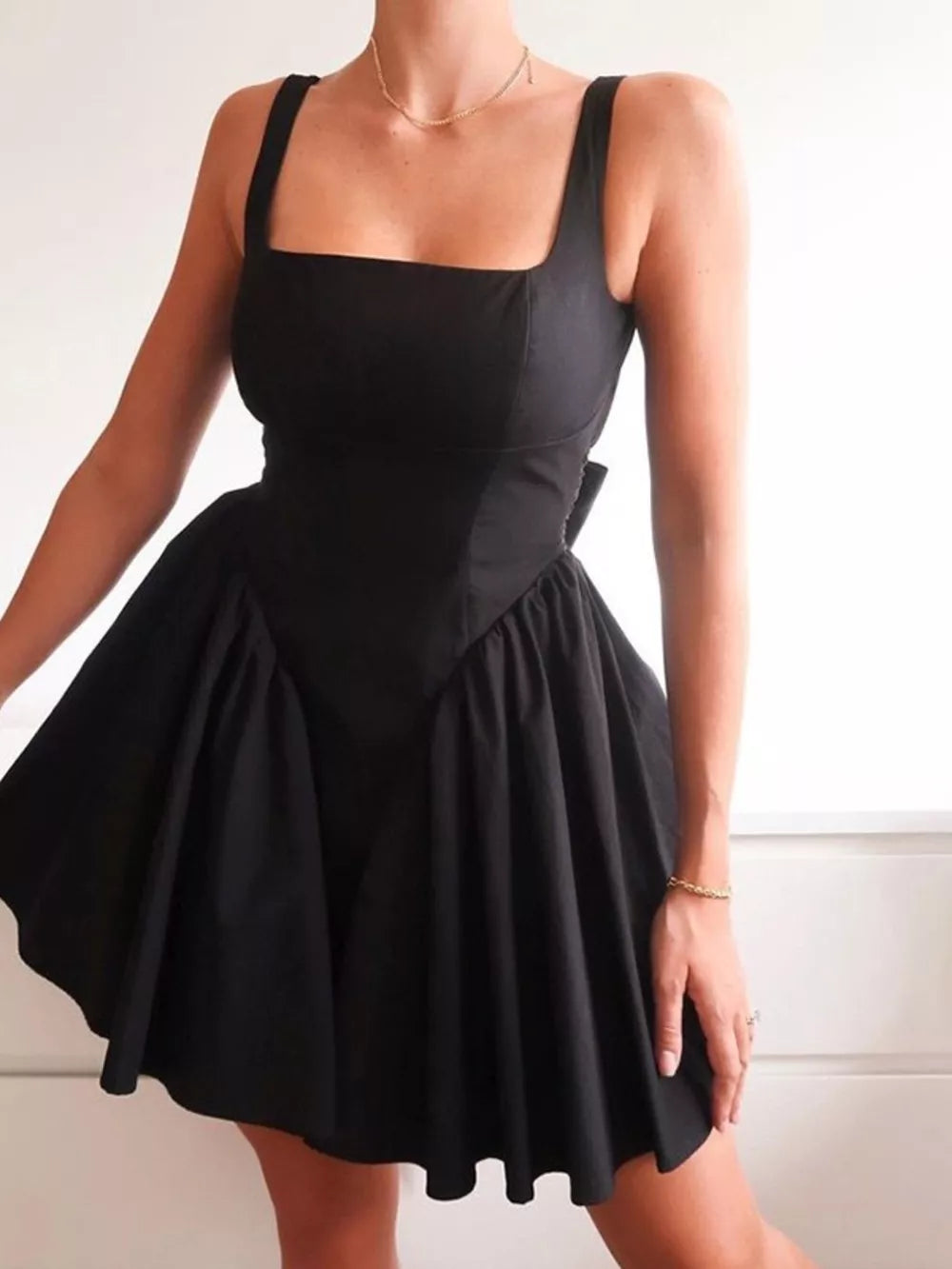 Black backless mini dress with square neckline, flared skirt, and bow detail.