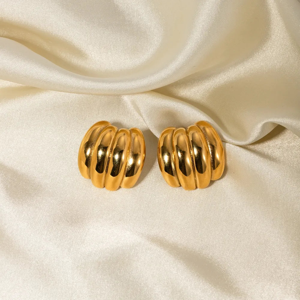 Sculptural ribbed gold earrings with a polished finish on a satin background.