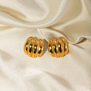 Sculptural ribbed gold earrings with a polished finish on a satin background.