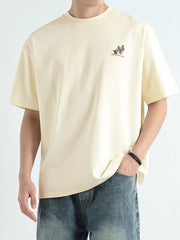 Men's relaxed fit graphic tee in apricot cotton with a small embroidered design and text.
