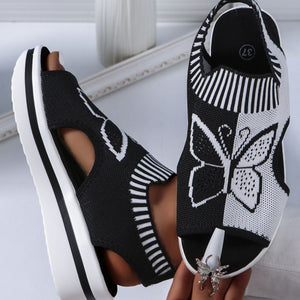 Chic black open-toe wedge sandals with white butterfly motif mesh detail and chunky sole.