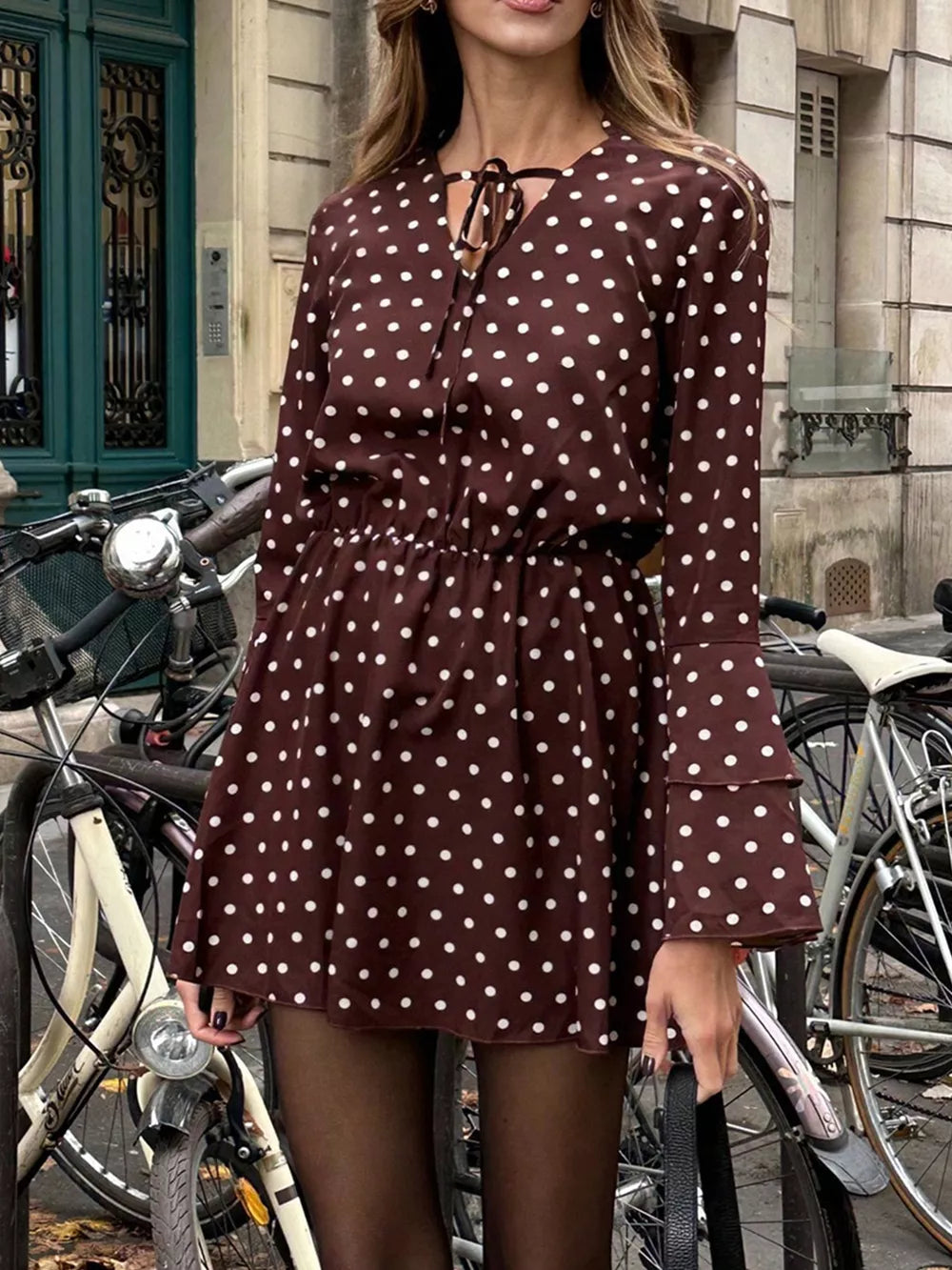 Brown polka dot mini dress with V-neck tie detail and tiered bell sleeves.