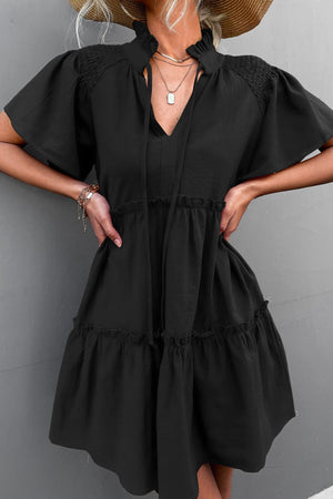 Black tiered ruffle sleeve trapeze dress with smocked bodice and tie neck.