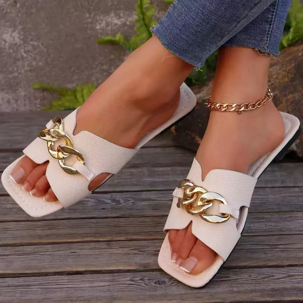 White slide sandals with gold chain detail and square toe.