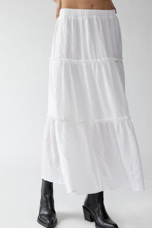 Tiered cotton maxi skirt in white with ruffled tiers, styled with black boots.