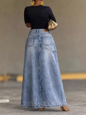 Asymmetrical high-waisted denim maxi skirt in light wash with visible back pockets and a raw hem.
