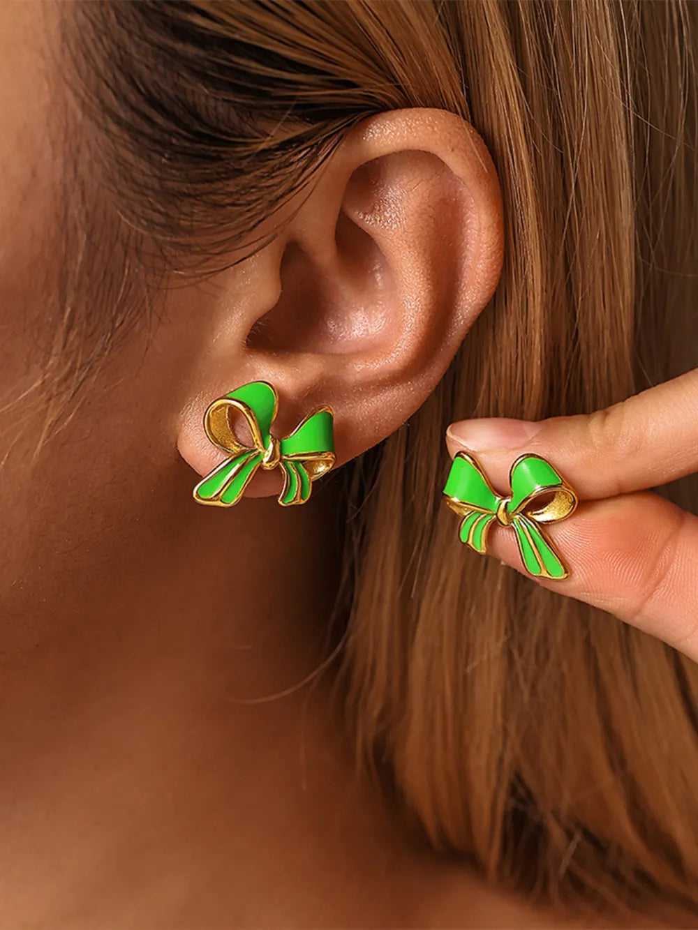 Green enamel bow stud earrings with gold detailing on a model's ear.