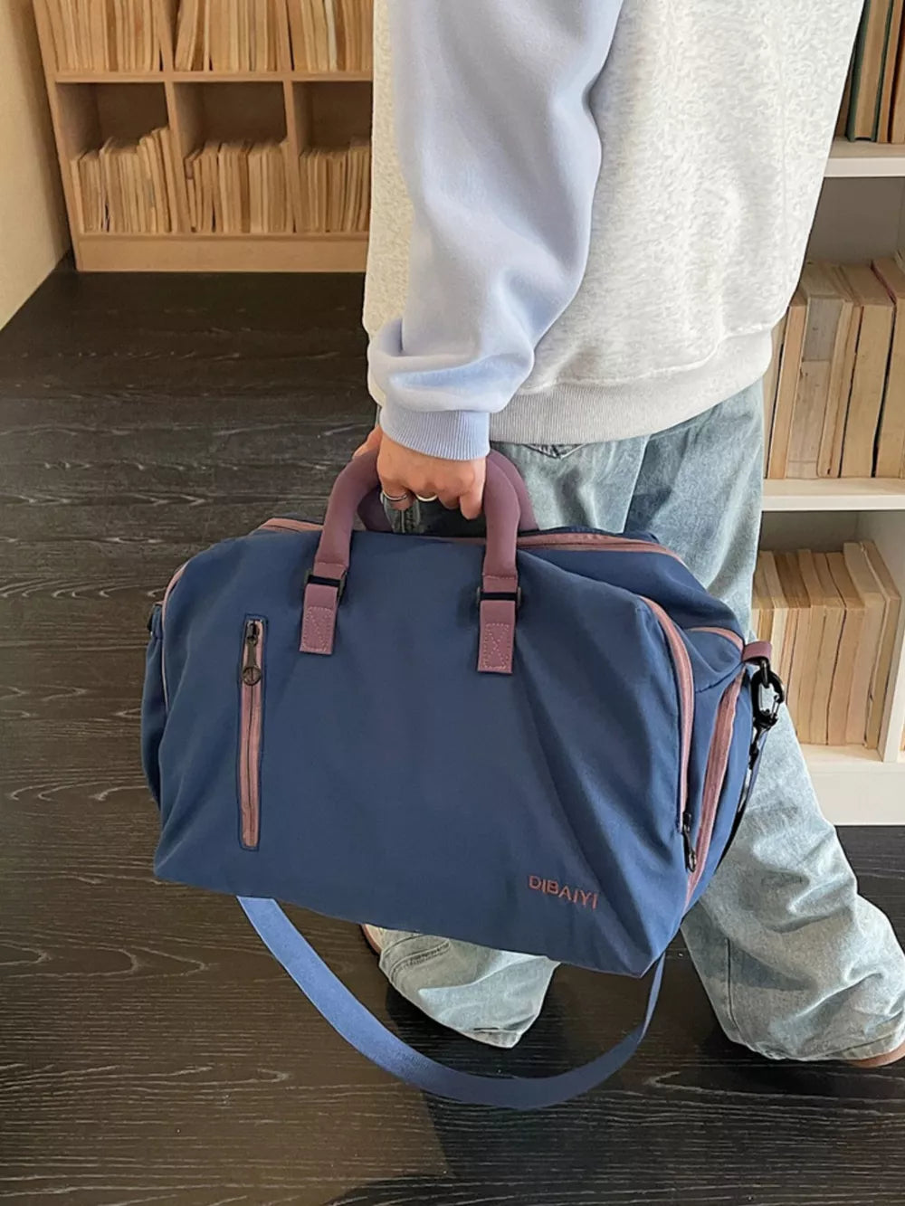 Blue travel organizer bag with pink accents and adjustable strap, held by a person.