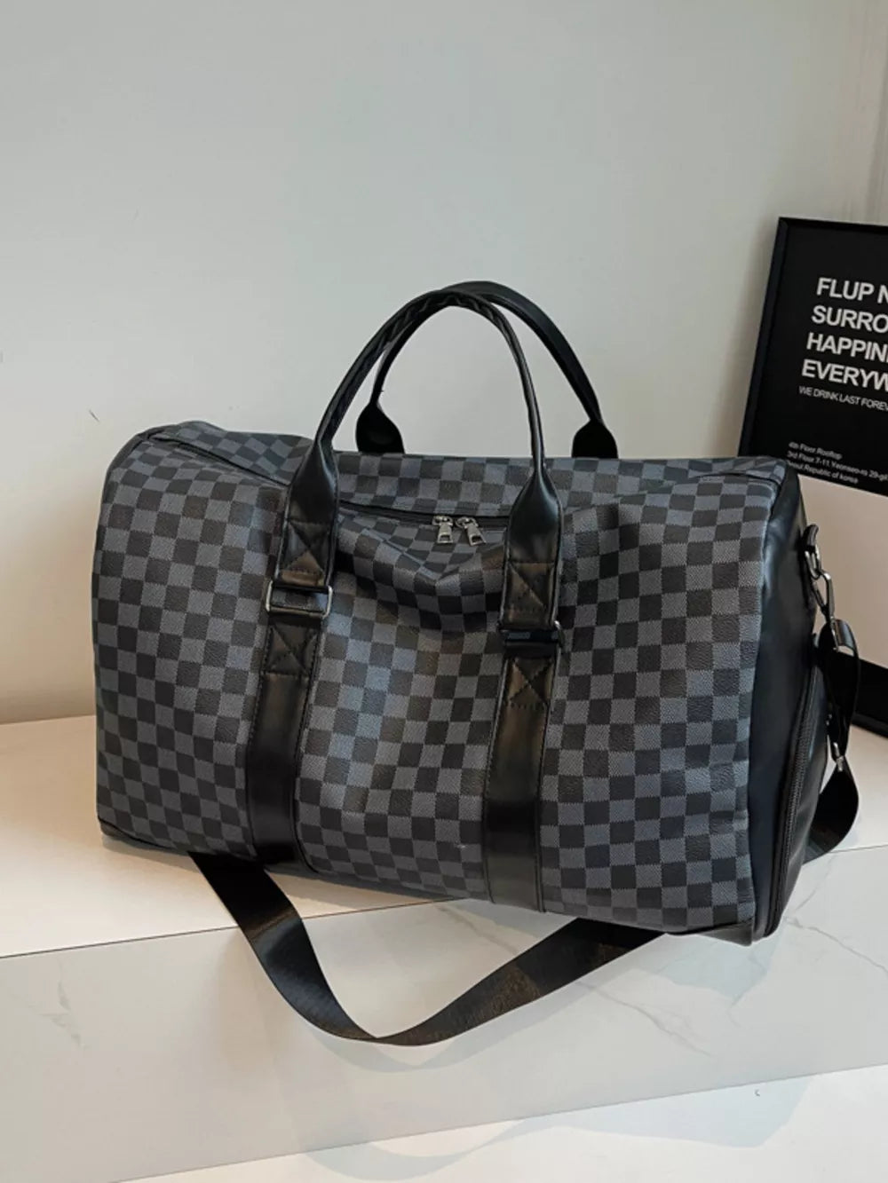 Black checkered travel bag with leather accents and shoulder strap