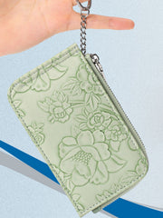 Sage green floral embossed mini wallet with zipper closure and keychain attachment.