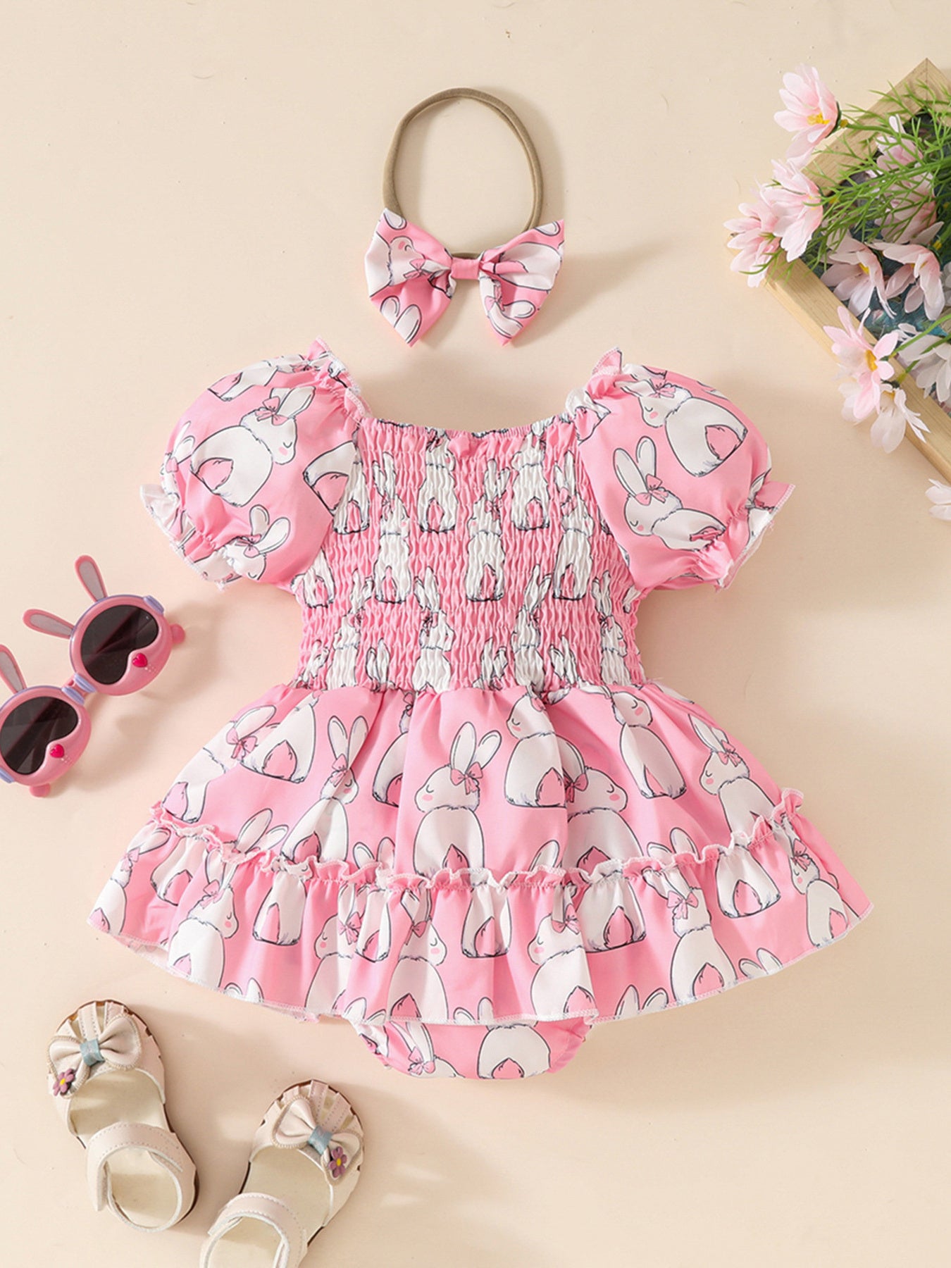 Pink bunny print baby dress with smocked bodice and ruffled hem, includes matching bow headband.