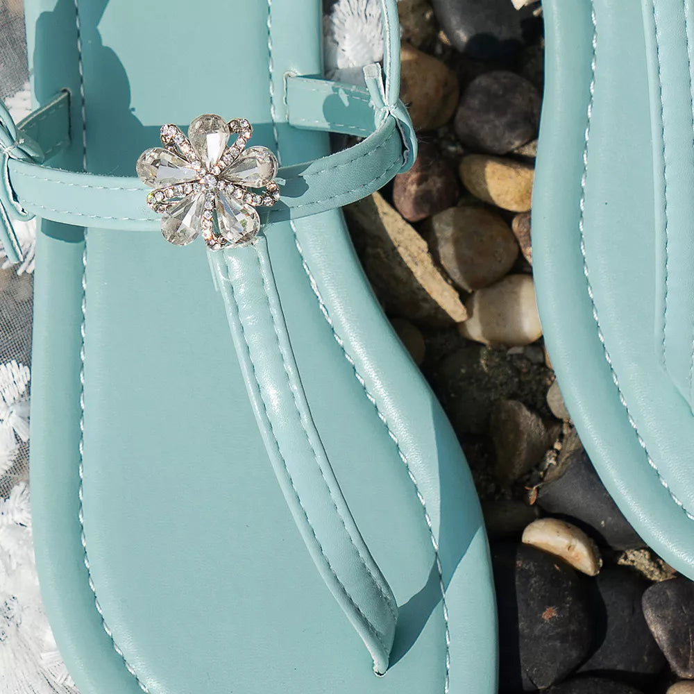 Lake blue flat sandals with floral gem embellishment and ankle strap.