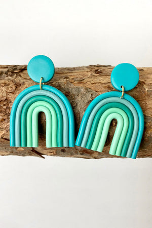 Aqua rainbow arch clay earrings with multiple shades of blue and green.