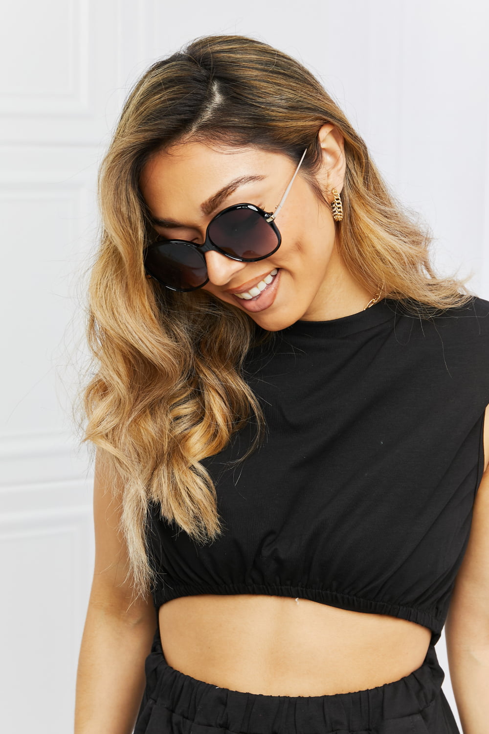 Oversized round black sunglasses with gold accents on a smiling woman.