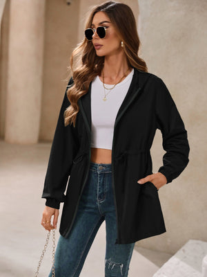 Black hooded jacket with cinched waistline and zip front, styled with a white crop top and jeans.