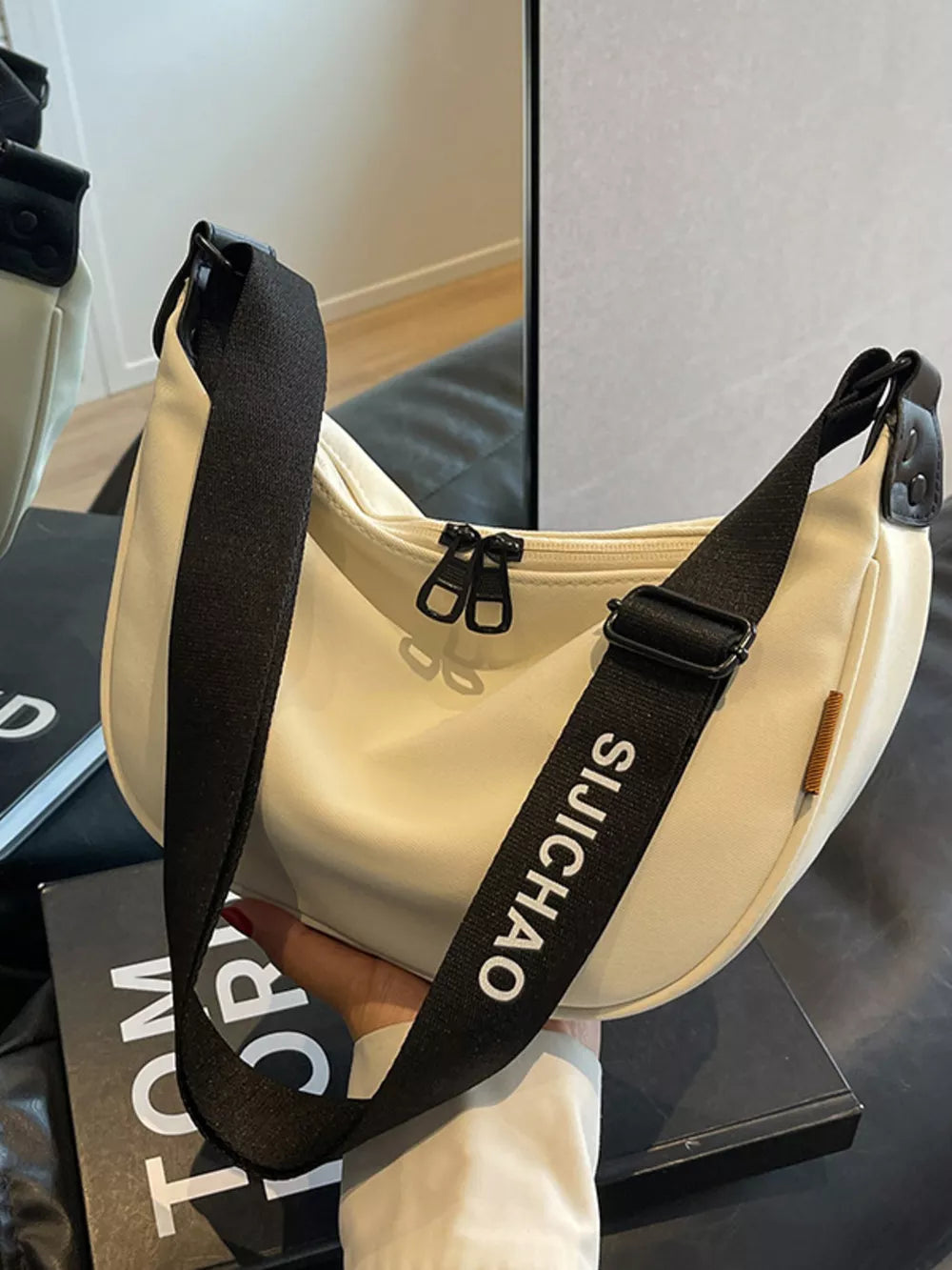 White crescent crossbody bag with black strap featuring white text