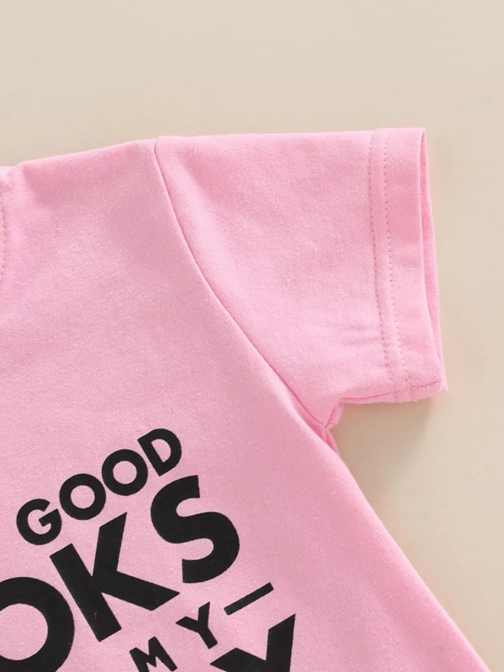 Pink cotton baby tee with black "GOOD LOOKS MY..." graphic print