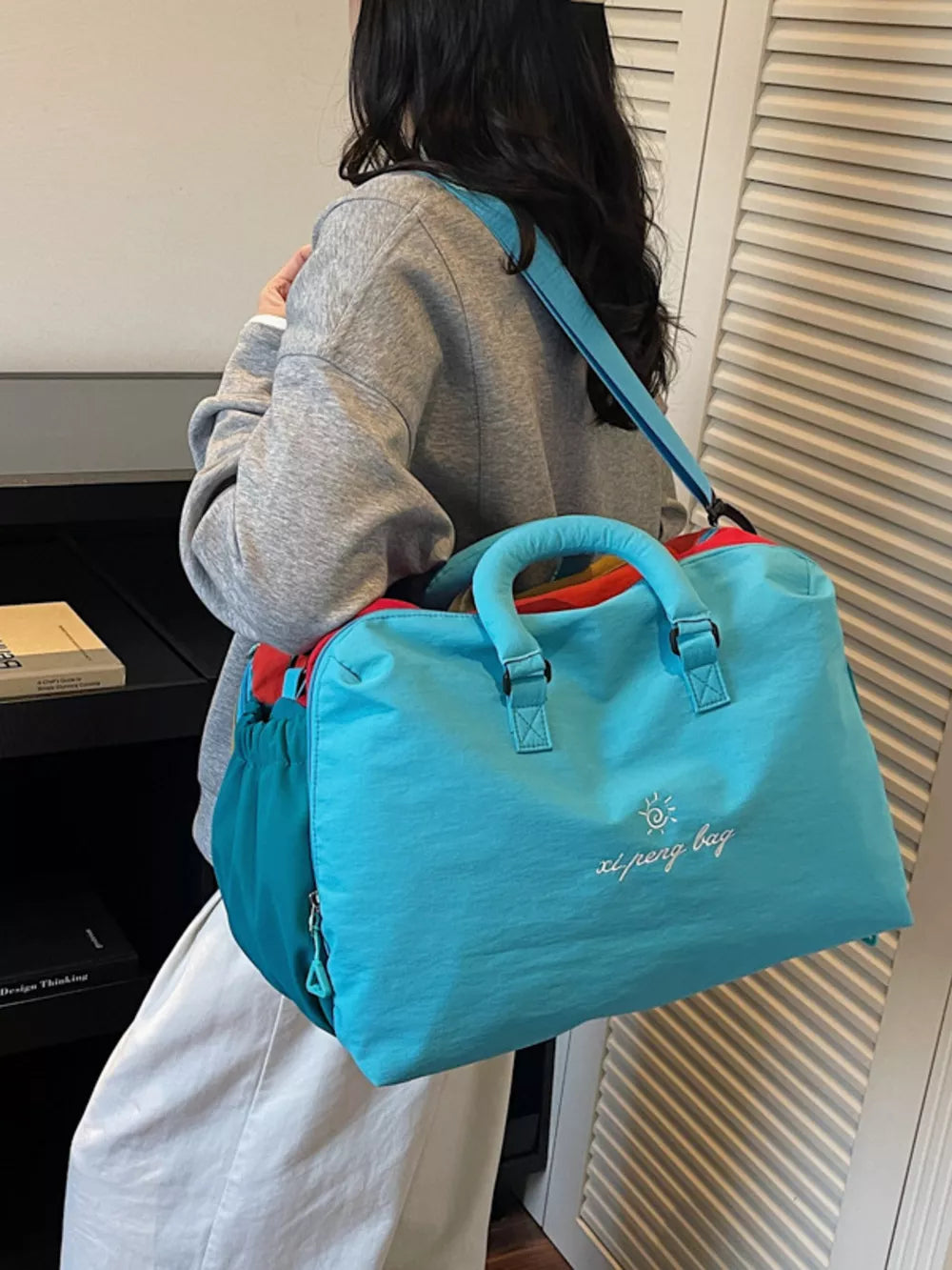 Blue duffel bag with embroidered sun and text, dual handles, and crossbody strap.