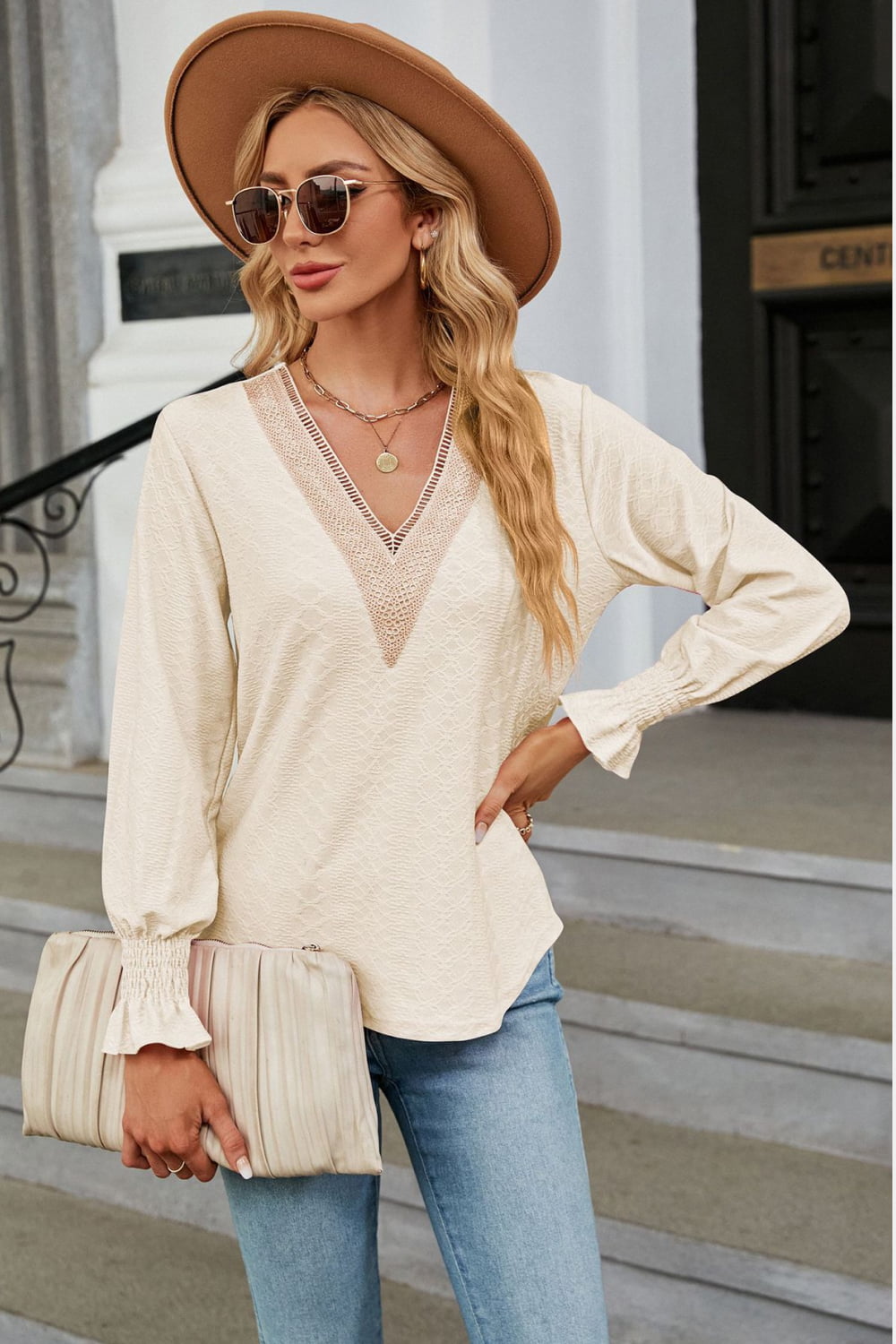 Cream textured V-neck blouse with lace trim and smocked cuffs.
