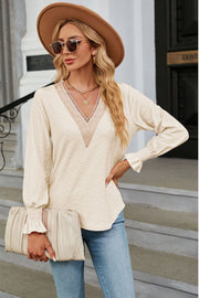 Cream textured V-neck blouse with lace trim and smocked cuffs.