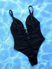 Black one-piece swimsuit with plunge neckline, ring detail, lace-up back, and ruched sides.