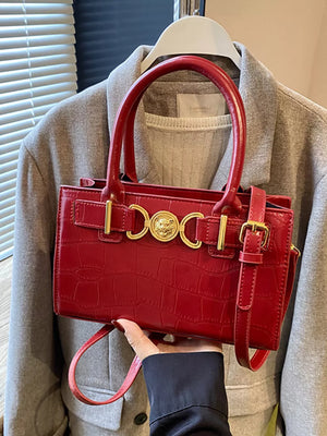 Red crocodile-textured crossbody bag with gold hardware and top handles.