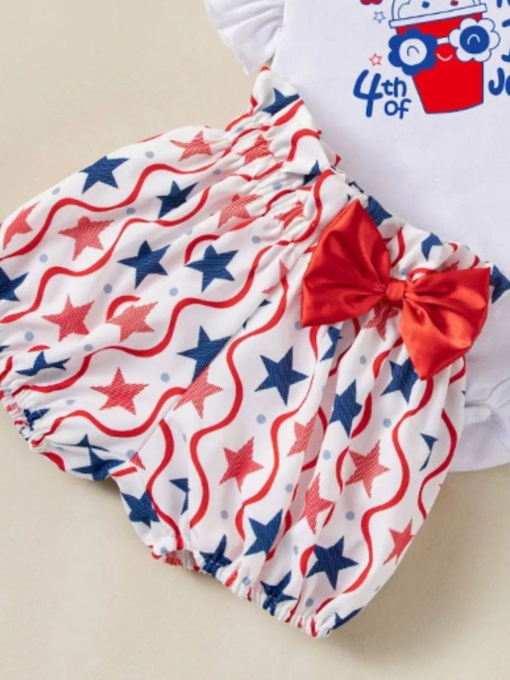 Baby outfit set with red, white, and blue star pattern bloomers and a red bow.