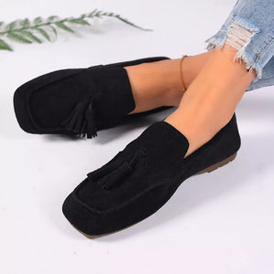 Black suede slip-on loafers with tassel detail and square toe.