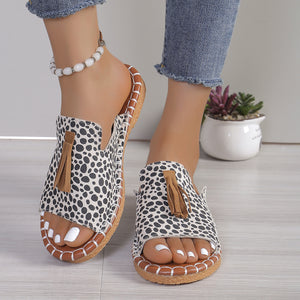Open-toe slide sandals in white leopard print with tassel detail and decorative stitching.