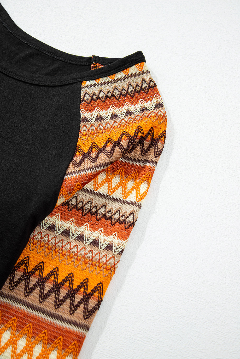Black raglan tee with orange, brown, and cream Aztec patterned sleeves.
