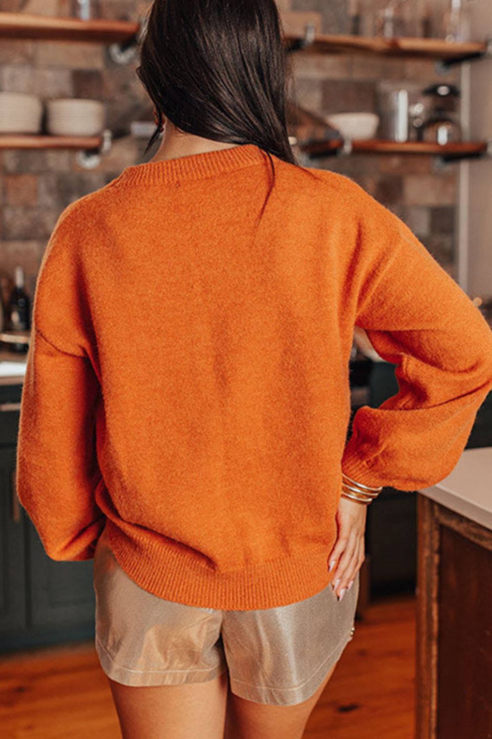 Orange knit sweater with crew neck and balloon sleeves, styled with metallic shorts.