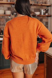 Orange knit sweater with crew neck and balloon sleeves, styled with metallic shorts.