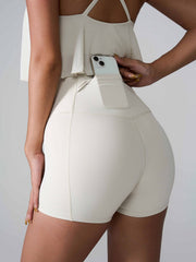 Cream active shorts with sculpted pocket detail and phone storage, high-waisted fit.