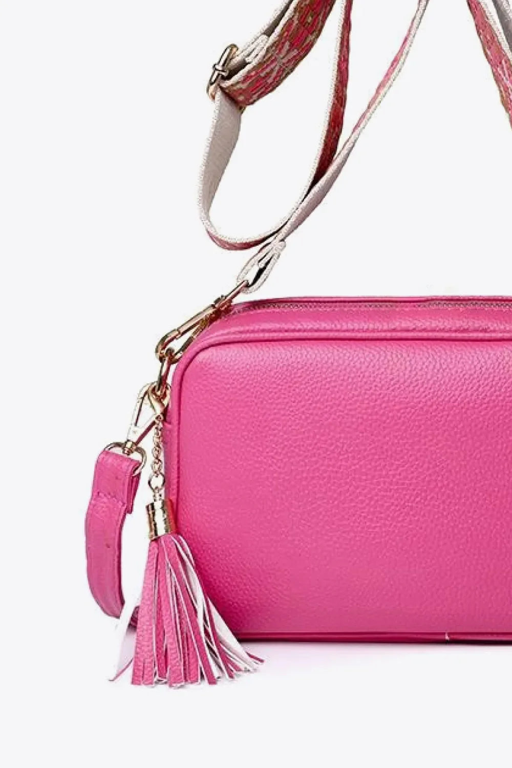 Textured crossbody bag in fuchsia pink with a multi-color tassel detail and patterned strap.
