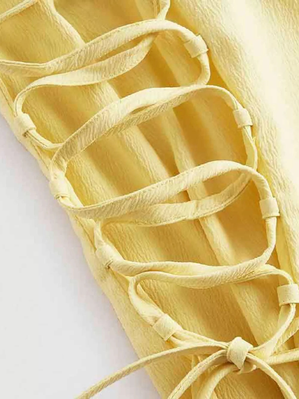 Light yellow cami dress with crisscross lace-up detail and textured fabric.