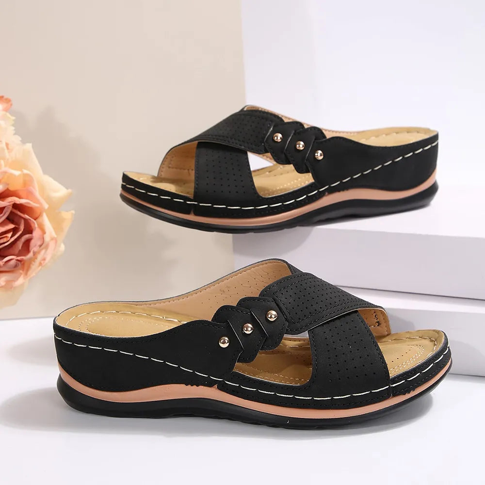 Black perforated cross-strap comfort sandals with decorative flower detail and white stitching.
